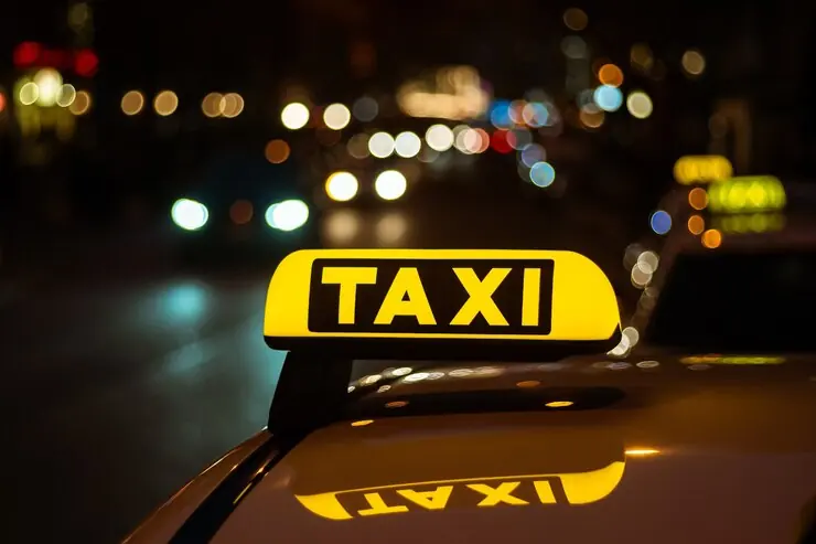 A yellow TAXI light lit on a car's roof, at night