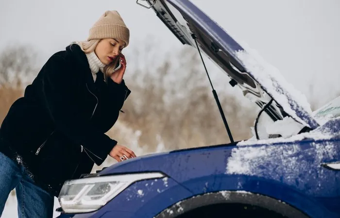 A woman calling for help beside a car with its bonnet up, in winter, in the snow