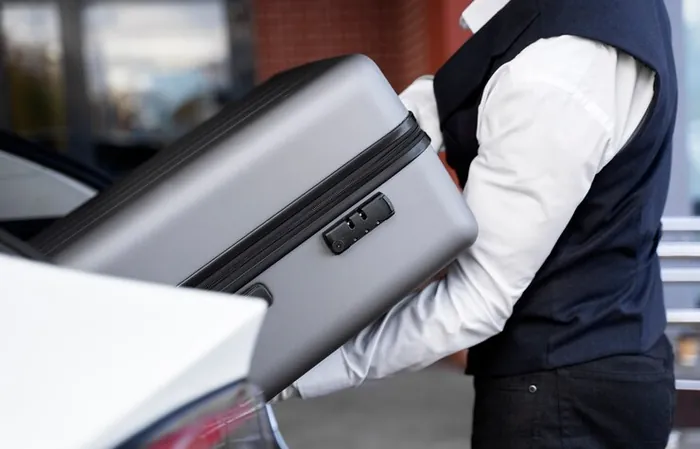 A driver placing a suitcase in the car's boot