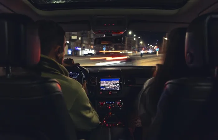 A driver at the wheel at night, seen from the back seat, city lights in the windscreen